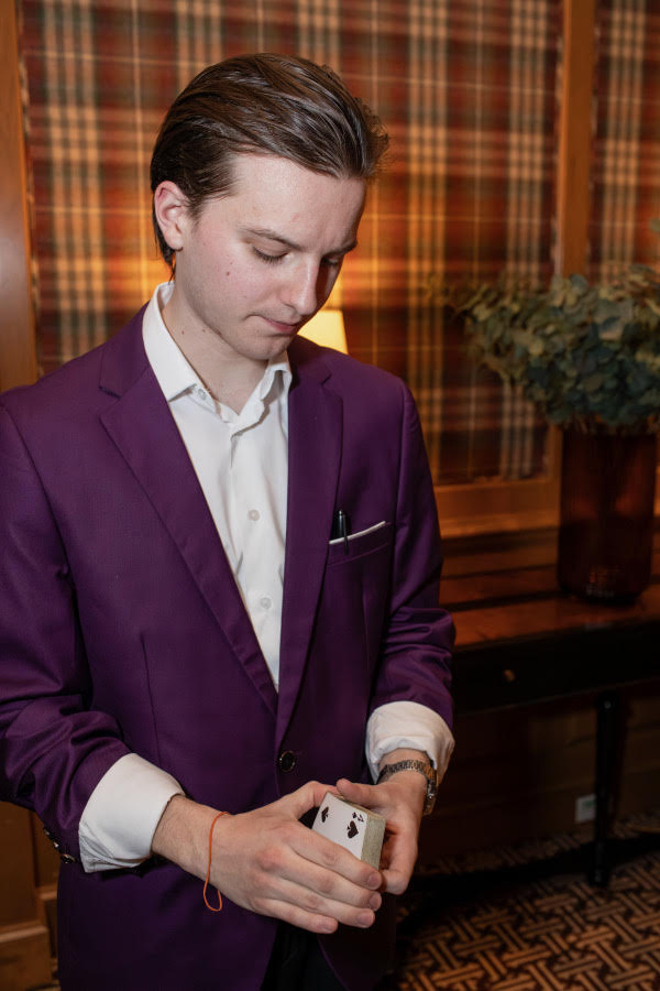Griffin in a purple suit performing a card sleight at an elegant event